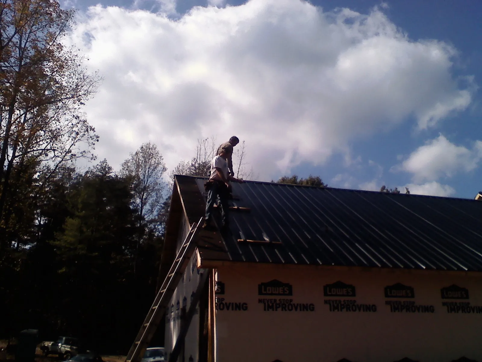 Roofer fastening dark metal panels high against a cloudy sky, from a Roof Inspection job in Yacolt